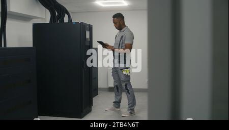 L'ingénieur professionnel en uniforme de sécurité utilise l'ordinateur tablette numérique pour analyser et mettre en place le système d'énergie. Spécialiste afro-américain masculin travaille sur une usine de fabrication moderne. Concept d'industrie lourde. Banque D'Images