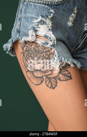 Jeune femme avec la cuisse tatouée sur fond vert, gros plan Banque D'Images