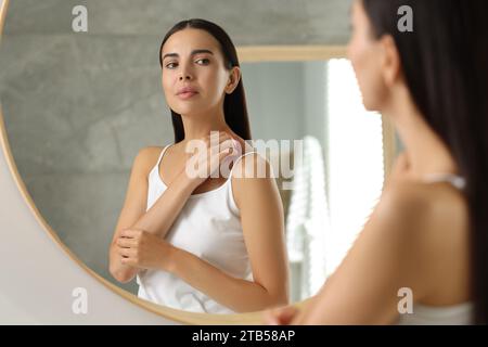 Souffrant d'allergie. Jeune femme grattant sa peau près du miroir dans la salle de bain Banque D'Images