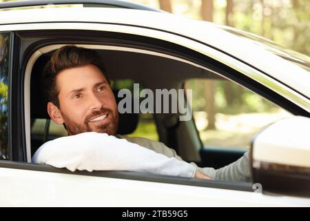 Homme barbu heureux regardant par la fenêtre de la voiture, vue de l'extérieur. Bon voyage Banque D'Images