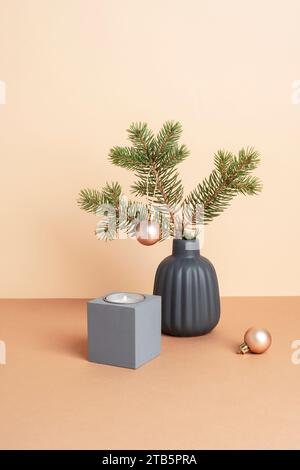 Branche d'épicéa dans un vase en céramique grise, bougie et boule de Noël sur table beige. Concept de Noël minimal Banque D'Images