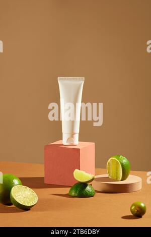 Un tube cosmétique non étiqueté est affiché sur une plate-forme rose avec du citron frais. Fond marron minimaliste. Espace sophistiqué pour la présentation des produits Banque D'Images