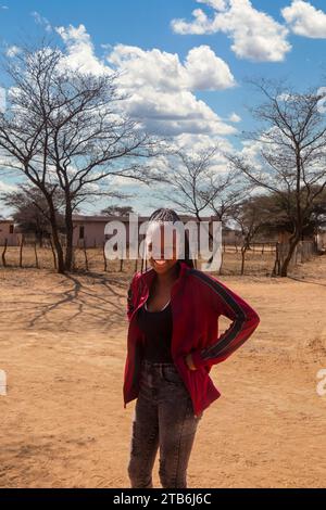 village, jeune fille africaine avec de longues tresses et un sourire toothy, maison de village en plein air Banque D'Images