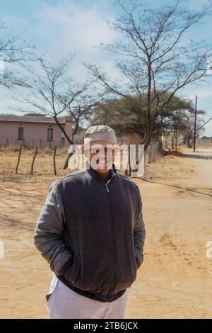 villageois , heureux en surpoids jeune homme africain avec un chapeau marchant sur un chemin de terre dans le village Banque D'Images