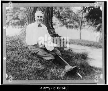 Warren Harding, portrait en pied, vêtu de vêtements de golf, assis sur le sol sous arbre, face à l'avant Banque D'Images