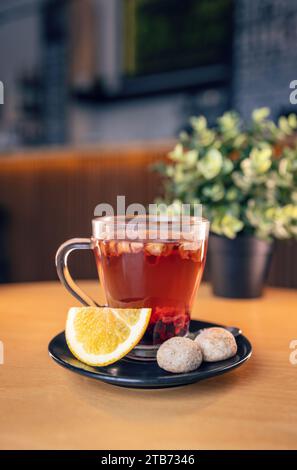 Infusion de fruits chauds dans une tasse transparente servie tranche de citron et deux biscuits Banque D'Images