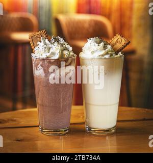 Verre de chocolat blanc chaud et noir avec crème fouettée. Boissons saupoudrées de poudre de cacao et servies avec biscuit Banque D'Images