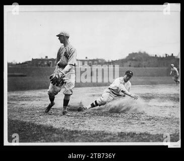 Bucky Harris des sénateurs de Washington glisse, alors qu'il vole avec succès la troisième base à la 7e manche d'un match de baseball contre les Red Sox de Boston ; le troisième joueur de base Joe Dugan regarde le ballon rouler Banque D'Images