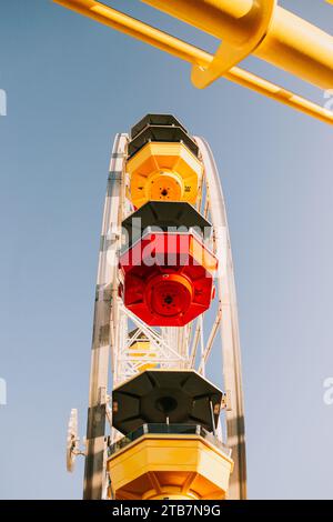 Gros plan d'une grande roue colorée vue d'en bas, avec des gondoles jaune vif et rouge sur un ciel bleu clair à Santa Monica Pier. Banque D'Images