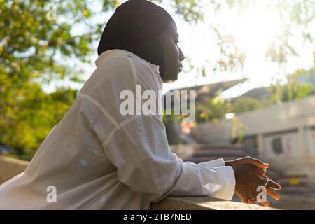 Vue de côté d'une femme d'affaires musulmane afro-américaine réfléchie en hijab noir regardant loin tout en se penchant sur la rampe dans la ville Banque D'Images