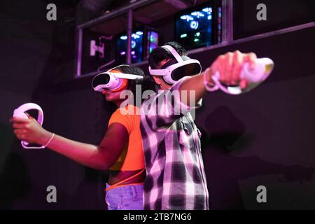 Les amis multiraciaux ont quitté un jeu de réalité virtuelle, chacun portant des casques VR et tenant des manettes, immergé dans une aventure numérique Banque D'Images