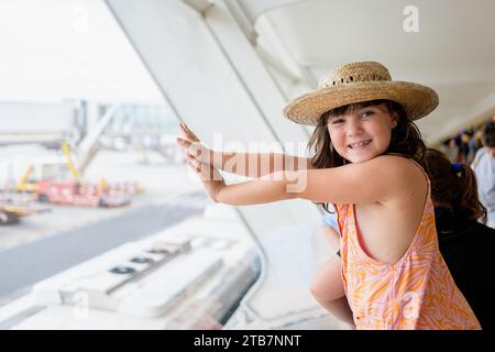 Vue latérale d'une fille voyageur sans visage portant un chapeau de paille et des occasionnels regardant la caméra tout en contemplant l'avion sur la voie de circulation à travers la fenêtre de l'aéroport Banque D'Images