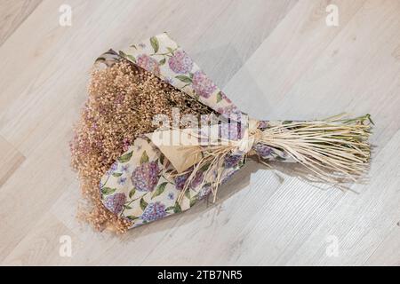 D'en haut délicat bouquet fait à la main de fleurs séchées enveloppé dans du papier floral reposant sur un fond en bois clair Banque D'Images