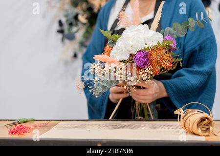 Personne méconnaissable fabriquant un bouquet, arrangeant des fleurs sur une table en bois, avec ficelle et ciseaux à proximité Banque D'Images