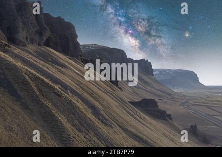 Vue majestueuse de la voie lactée étirant son arc stellaire sur un paysage déserte et éclairé par la lune tandis que des collines se dressent silencieusement sous un ciel étincelant de Coun Banque D'Images