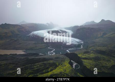 Vue aérienne d'une route sinueuse serpentant vers un glacier au milieu du paysage brumeux et accidenté du parc national de Vatnajokull en Islande. Banque D'Images