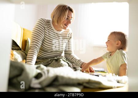 Une scène réconfortante avec une mère souriante s'engageant avec son tout-petit curieux dans un cadre lumineux et confortable à la maison. Banque D'Images