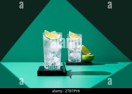 Deux verres de gin tonic avec des tranches de citron vert projettent des ombres intéressantes sur un fond vert, soulignant un sentiment de rafraîchissement. Banque D'Images