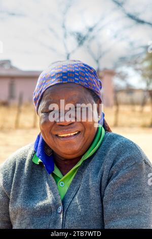 villageois, vieille femme africaine riant d'une bonne blague, maison et chemin de terre en arrière-plan Banque D'Images