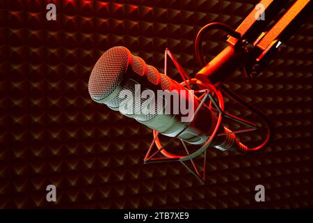 Vue rapprochée capturant les détails d'un microphone de studio professionnel sur un support antichoc rouge, placé contre la mousse insonorisante d'un Recor bien éclairé Banque D'Images
