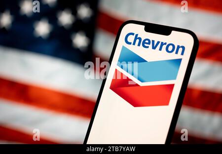 Le logo Chevron est vu avec un drapeau américain en arrière-plan dans cette illustration photo le 13 mars 2023 à Varsovie, Pologne. Banque D'Images