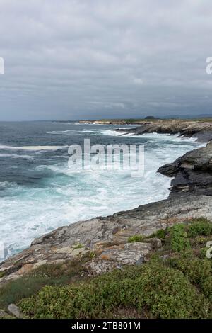 l'océan turbulent s'écrase contre une côte rocheuse sous un ciel gris nuageux, avec une petite île visible au loin Banque D'Images