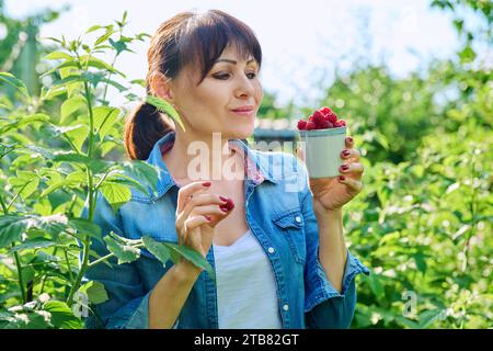 Femme heureuse dans le jardin des framboisiers, avec une tasse de framboises mûres Banque D'Images