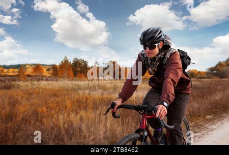 Cycliste fait du vélo de gravier sur un sentier dans le champ. Homme en casque une lunettes de cyclisme en plein air. Banque D'Images