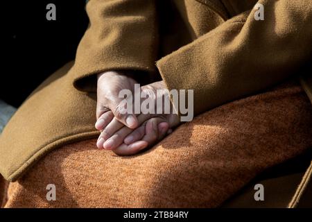 Les mains d'une femme sont serrées avec les doigts entrelacés et couchées doucement dans une pose calme et détendue sur ses genoux. Banque D'Images