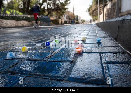Les bouchons de bouteilles d'eau en plastique multicolores reposent sur une rue mouillée et pavée pendant la course du marathon de Jérusalem. Banque D'Images