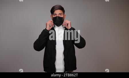 Un jeune homme portant un masque sur un fond gris. Banque D'Images