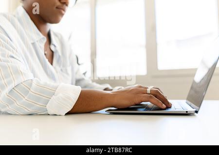 Photo recadrée d'une femme afro-américaine à l'aide d'un ordinateur portable, l'employée est en train de taper sur le clavier, répondre à des e-mails, femme freelance multiraciale en tenue décontractée travaillant à distance du co-working Banque D'Images