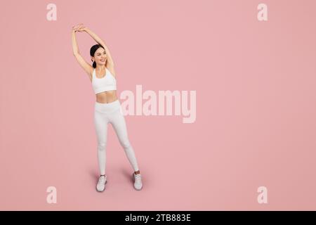 Mince dame caucasienne en vêtements de sport faisant des étirements de bras et des exercices d'échauffement isolés sur fond rose, pleine longueur Banque D'Images