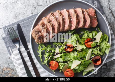 Steak grillé Tagliata di Manzo servi avec roquette, tomates cerises et parmesan en gros plan dans une assiette sur la table. Vue de dessus horizontale depuis abo Banque D'Images