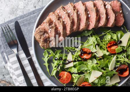 Tagliata de steak de bœuf avec roquette, parmesan, tomates cerises et gros plan balsamique sur une assiette sur la table. Vue de dessus horizontale Banque D'Images