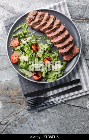 Tagliata di manzo Steak de bœuf à l'italienne servi avec roquette, tomates cerises et parmesan gros plan dans une assiette sur la table. Vue verticale de dessus à partir de Banque D'Images