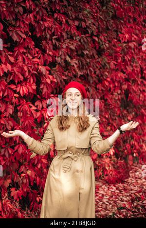 fille aux cheveux roux dans un béret rouge sur un fond d'un mur de feuilles rouges Banque D'Images