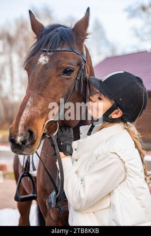 Belle jockey blonde professionnelle embrassant le cheval brun à la ferme. Amitié avec le cheval Banque D'Images