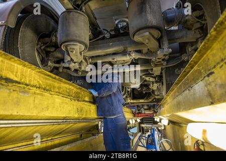 Garage, atelier de réparation pour poids lourds : mécanicien dans la fosse d'inspection travaillant sur le moteur d'un camion Scania Banque D'Images