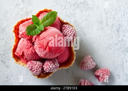 Boules de délicieuses glaces fraîches à la framboise décorées de framboises surgelées et de feuilles de menthe verte, servies dans un bol à gaufres Banque D'Images