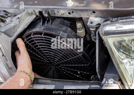 Un homme répare un ventilateur de refroidissement du moteur sous la grille du radiateur d'une voiture. Entretien et réparation de machines. Banque D'Images