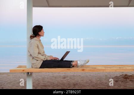 Jeune femme indépendante réfléchie triste assise sur un banc de plage regardant le beau lac et les montagnes arrière-plan Banque D'Images
