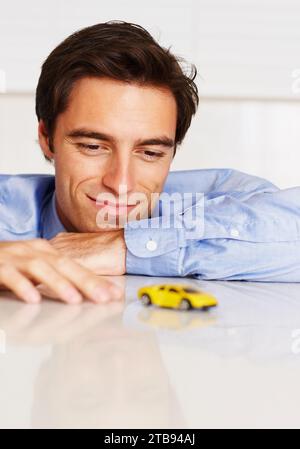 Voiture jouet, entreprise et homme avec un sourire, bureau et employé avec bonheur, joyeux ou entrepreneur. Personne, agent ou consultant jouant avec le véhicule Banque D'Images