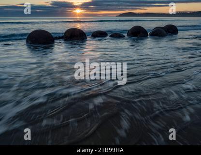 Marée entrante au lever du soleil avec les rochers Moeraki dans le surf le long d'une portion de Koekohe Beach sur l'île du Sud de la Nouvelle-Zélande Banque D'Images