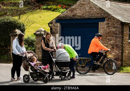 Hommes et femmes cyclistes à vélo électrique et bavarder avec des femmes avec des bébés dans des landaus à Hartley. Kirkby Stephen, North Pennines, Cumbria Banque D'Images