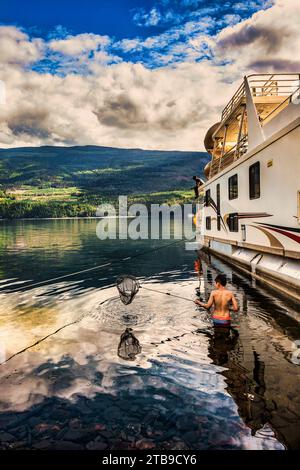 Une famille profitant de vacances en péniche aménagée sur le rivage du lac Shuswap avec un homme pêchant sur le pont de la péniche et un garçon ... Banque D'Images