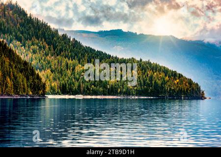 Une péniche garée le long de la rive du magnifique lac Shuswap avec des rayons du soleil créant un éclairage spectaculaire et des reflets sur les montagnes et la wa... Banque D'Images