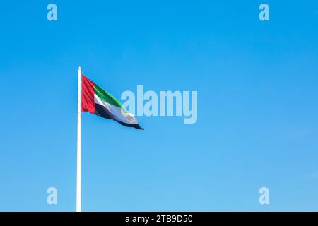 Agitant le drapeau des Émirats arabes Unis sur un mât contre un ciel bleu Banque D'Images