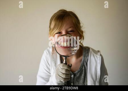 Fille souligne son sourire avec une loupe sur un fond blanc ; Studio Banque D'Images