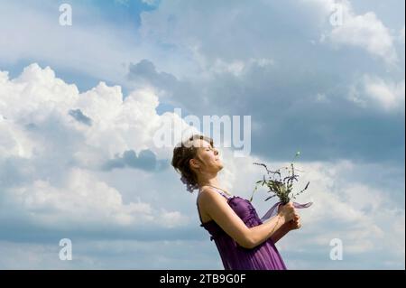 Femme tenant des fleurs fermement dans ses mains contre un ciel rempli de nuages ; Firth, Nebraska, États-Unis d'Amérique Banque D'Images